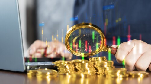 Magnifying glass focusing on gold coins with candlestick chart, financial analysis, trading and investment